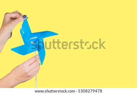 Closeup view of female hands with blue manicure holding blue pinwheel isolated on bright yellow background with copyspace. Horizontal color photography.