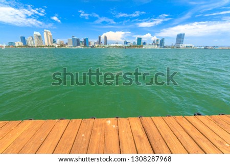 Empty wooden footpath walkway in front of San Diego skyline. Wooden desk background on sea beach in San Diego Bay. Urban downtown cityscape from Coronado Island. Sunny with blue sky. Copy Space.