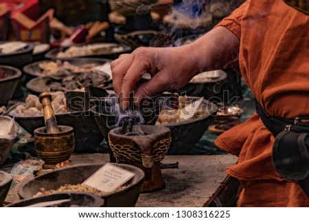 Shaolin master monk during herbal tea preparation. Calmness and silence, spiritual meditation concept. Incense stick and smoke close up. Orange robe, brass and gold bowls.  Royalty-Free Stock Photo #1308316225