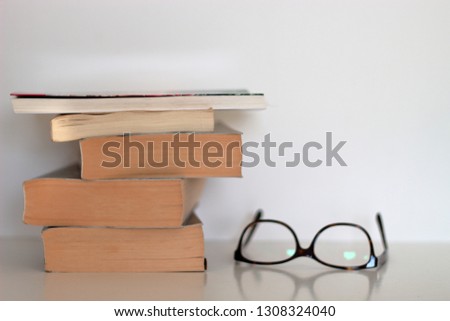 Stack of books and eyeglasses on White table with White background.