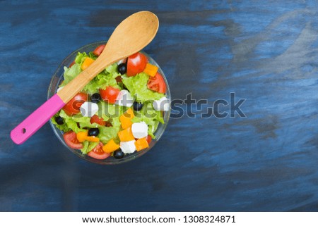Greek salad in a glass bowl on black or dark gray wooden or metal table