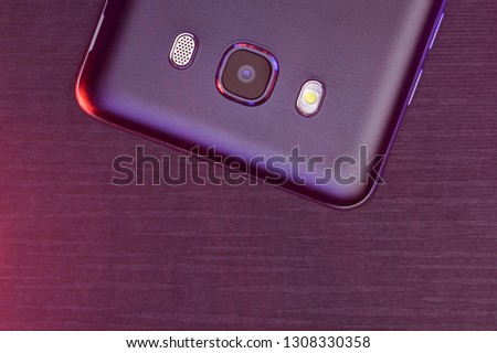 Black smartphone on dark background.  A fragment of the cell phone case in black with pink and purple backlight. 