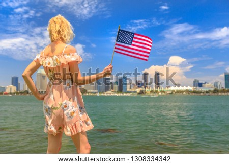 Tourism and travel in California, West Coast, USA. Blonde lady looking San Diego skyline with American flag waving from Coronado Island. Tourist woman in summer holidays. Cityscape in San Diego Bay.