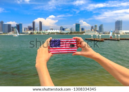 Tourism and travel in California, West Coast. Mobile phone with American flag cover taking photos of San Diego By skyline. Smartphone shoting in summer holidays from Coronado Island, USA.
