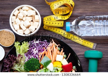 Fresh vegetable salad and healthy food for sport equipment for women diet slimming with measure tap for weight loss on wookd background. Healthy Sport Concept