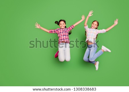 Full length body size photo two little age she her girls hand arm up jump high school competition cheerleaders wear casual jeans denim checkered plaid shirts isolated green vibrant vivid background