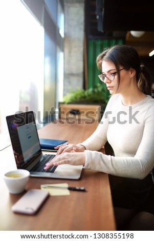Hipster girl experienced business planning expert working on laptop computer while sitting in modern office interior. Female with cool look creative web content writer checking e-mail on notebook 