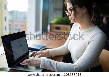 Woman in glasses with stylish look skilled marketing specialist checking e-mail on laptop computer, sitting at workstation in co-working space. Business female received notification on notebook 