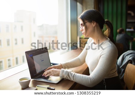 Young female professional associate web editor working on laptop computer, sitting in coffee shop during recreation time in holidays. Woman college student having online education via netbook device 