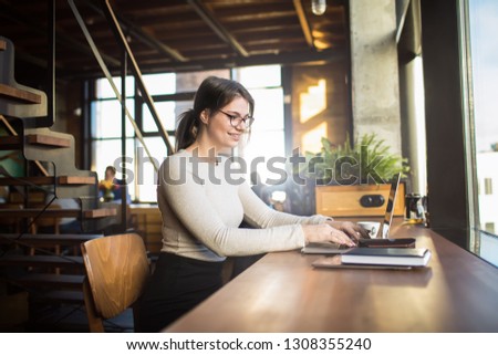 Joyful woman having online training course via pc laptop computer while sitting in coffee shop. Smiling skilled female in glasses chatting via netbook during leisure time in co-working cafe 