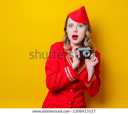 Portrait of charming vintage stewardess wearing in red uniform with photo camera. Isolated on yellow background.