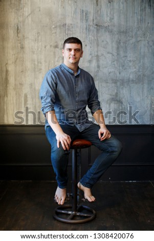 Young man weared in casual on background of gray wall. Young male indoor seat on background of concrete wall