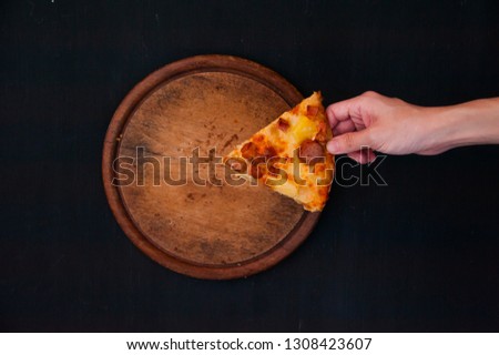 Top view of hand taking a thin crispy pizza on wooden tray with black background