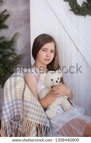 Cute little blonde girl in white dress sits in an embrace with a bear. child opens a gift Christmas eve. Christmas atmosphere, comfort. Dreamy girl. Merry Christmas and happy holidays! New Year 2020. 