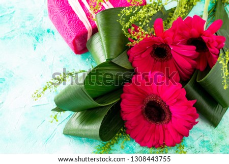 Mother's Day background or greeting card. Bouquet Red Flowers of gerbera and a present on a turquoise stone table. Copy space.
