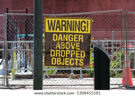 Warning Danger Above Dropped Objects large brown and yellow vinyl sign on chain length safety and security fence around a construction site in downtown Fort Lauderdale Broward County Florida. 