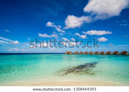 A row of water villas over the turquoise colored sea in a Maldives resort viewed from a beach in a sunny day