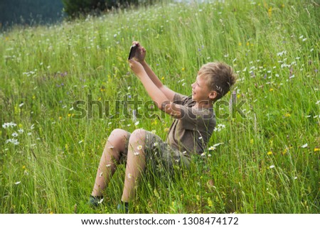 White handsome young kid taking selfie sitting at beautiful scenic meadow at countryside. Horizontal color photography.