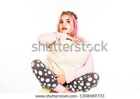 Amazing girl with pink curly hair playfully posing in cute pajama holding pillow and laughing to camera. Indoor photo of inspired young woman in night-suit isolated on white background