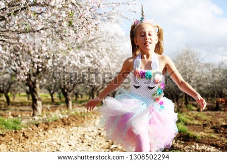 Girl in a unicorn costume jumps outdoors. Spring is around, apple trees are blooming.