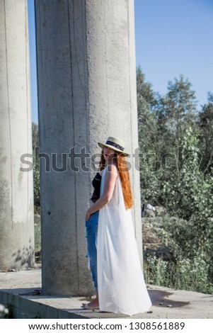 Silhouette of young redhead woman in hat and jeans near the column.