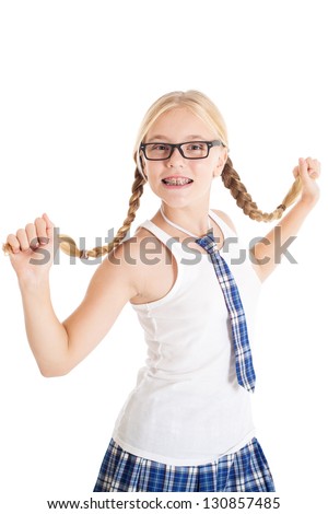 Schoolgirl blonde with two braids wearing a school uniform and black-framed glasses. Braces on teeth. Girl stretches aside their long braids. Studio shot, isolated on white background.