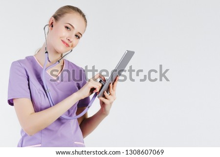 Girl doctor blonde gray background one beautiful listen stethoscope look tablet smiling positive. Online patient consultation.Treatment distance. Communication hospital.