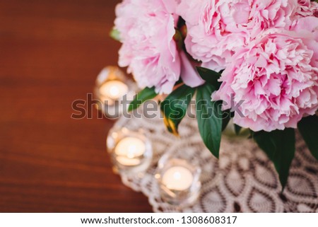 A bouquet of beautiful pink peony flowers in a vase on a table surrounded by candles. Copy space