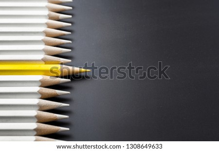 Business and design concept - lot of white pencils and one color pencil on black background. It's symbol of leadership, teamwork, success and unique.