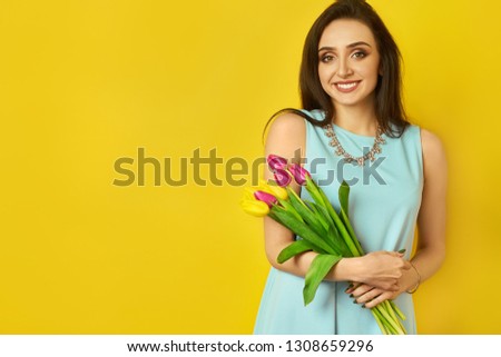 Fashion photo of a beautiful young woman with tulips in her hand .she dressed in a beautiful coat,  and T-shirt with stripes on the yellow background .Spring concept. March 8. beautiful girl.