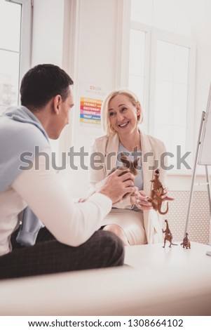 That is joke. Cheerful male person holding toy in his hands and listening to his therapist