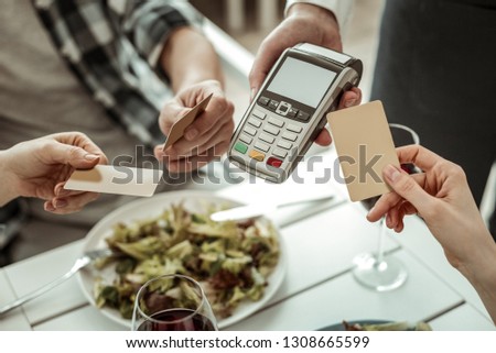 Lets pay. Competent waiter serving his clients and holding terminal for payments