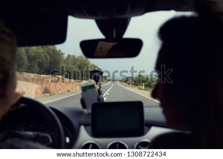 Selective focus on road. Close-up shot two female silhouettes traveling by automobile. Good view of long road with curves and signs. Young driver uses navigation on phone. Mock up for advertising.