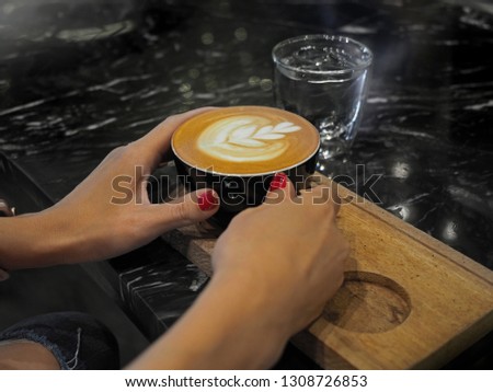 Woman hand with red manicure holding a cup of cappuccino coffee on a black granite counter bar. Selected focus.