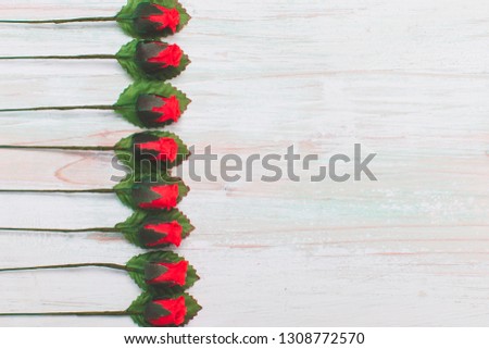 Valentine's day and Love concept, arrangement of beautiful fake red rose and leaf, orderly row on bright brown wooden background, copy space on bottom side, flat lay, top view greeting card style