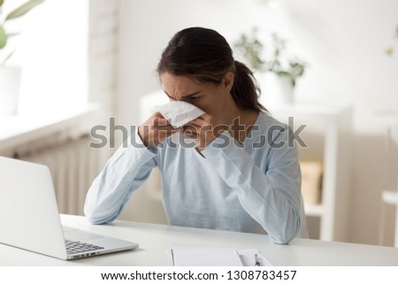 Unhealthy female sitting at workplace holding napkin sneezing and blowing her nose. Office worker is unable to work because of grippe. Person with chronic allergic rhinitis hard to breathe concept Royalty-Free Stock Photo #1308783457