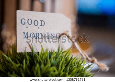 Close up image of GOOD MORNING label on green plant with blurred cake in the background. Selective focus.