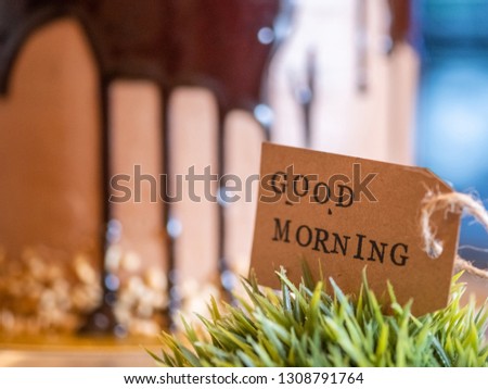 Close up image of GOOD MORNING label on green plant with blurred cake in the background. Selective focus.