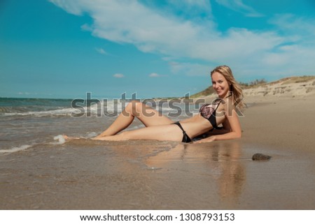 young blond woman in swimsuit at sea surf with foam lying, looking at camera