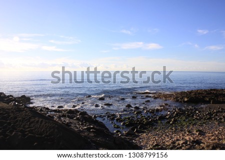 Rocky Beach in San Agustin on gran Canaria with bright Sun Shine and Blue Cloud Sky, blue water and waves