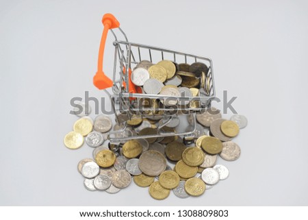 Financial, shopping, commerce, business concept. Excessive coin money and shopping cart with selective focus on isolated white background.                           
