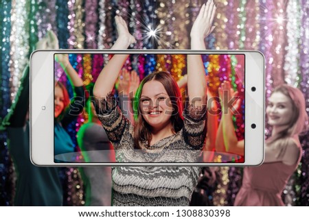 Young woman having dance party in night club, conceptual image with a smartphone