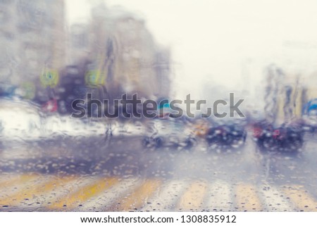 Blurred view through the windshield of a car with raindrops at a crossroad and pedestrian crossing.