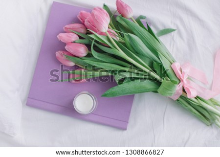 Wedding photo album with fabric cover, bunch of tulips, candle on white bed linen. Valentines Day concept. Feminine background, top view, flat lay.