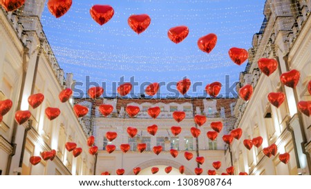 Happy Valentines Day concept - red heart shape balloons waving in the wind at city street festival. Warm illumination, evening time
