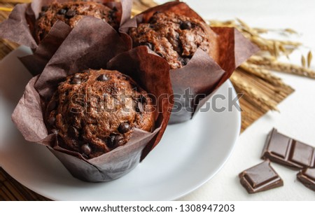 Three chocolate muffins on a white plate, on a Mat. Behind the wheat ears. Next chocolate bar.Macro picture.