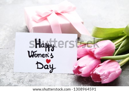 Text Happy Women's Day with pink tulip flowers and gift box on grey wooden table