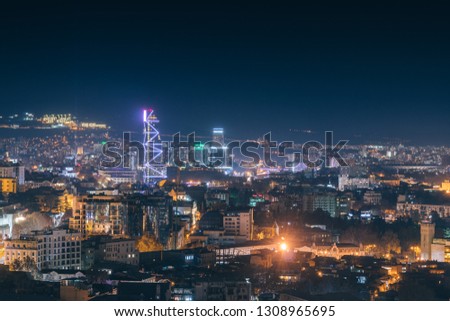 Panoramic view of the tourist part of the night Tbilisi. Blue light business center. Skyscraper among low urban development. Old town on the hills.