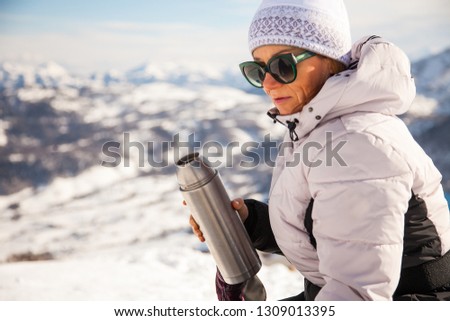 Adult woman with thermos of tea on mount top with spectacular view of snowy mountains on background. Bakuriani, Georgia, mount Kokhta