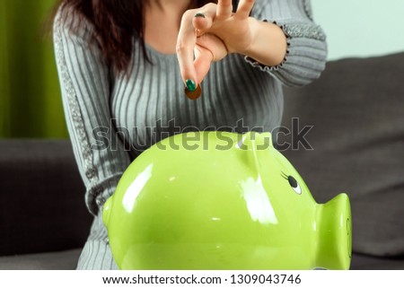Creative background, close-up girl's hand, throws a coin into the piggy bank in the form of a green pig. The concept of saving money, savings, pig piggy, family budget, copy space.